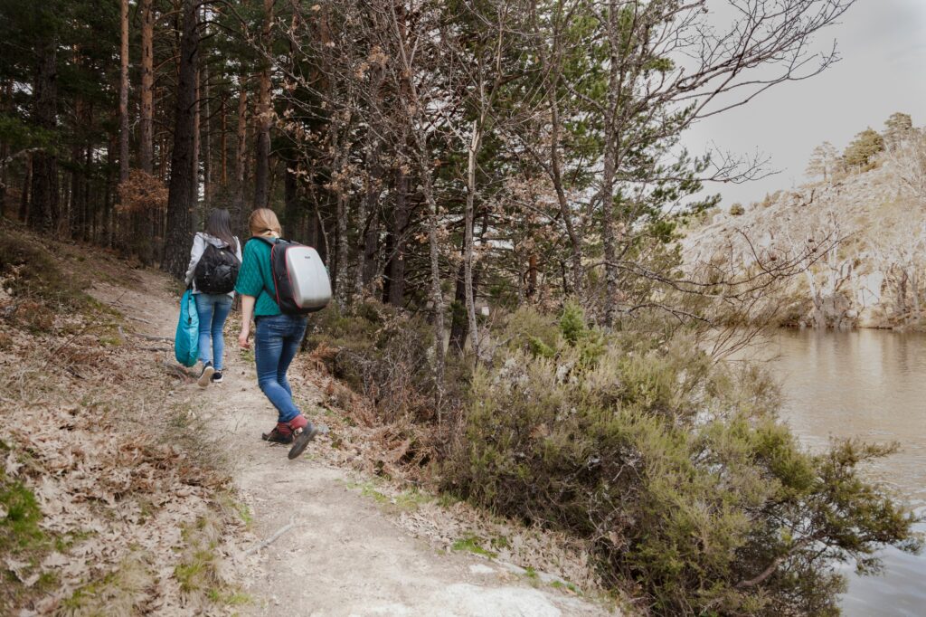 Two women hiking along a forest trail near a river, enjoying nature and searching for hiking trails near me.